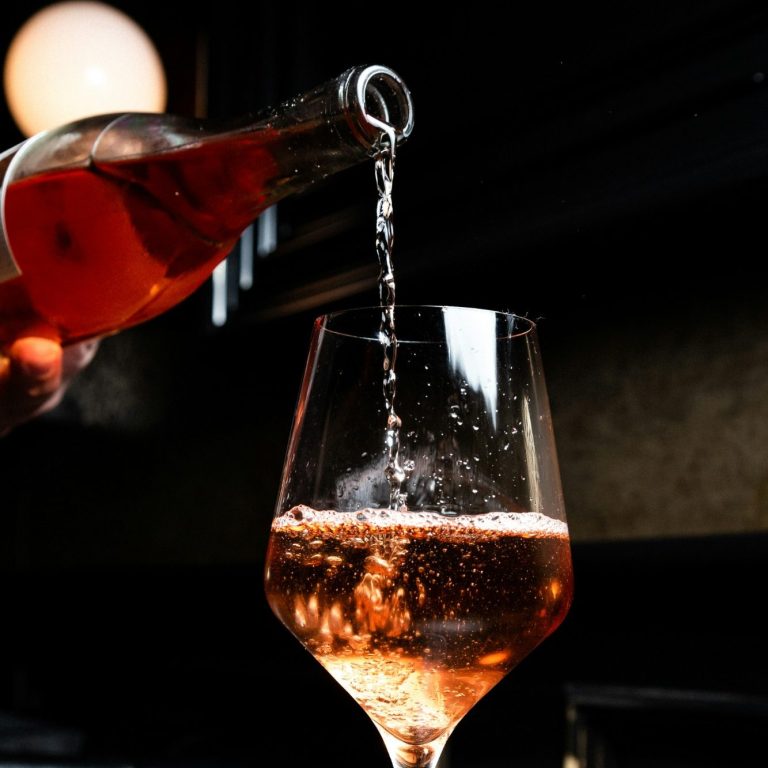 Ein Glas wird mit roséfarbenem Getränk aus einer Flasche gefüllt.